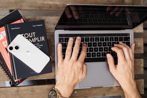 Mains sur le clavier d’un ordinateur portable, entourées de carnets et d’un téléphone